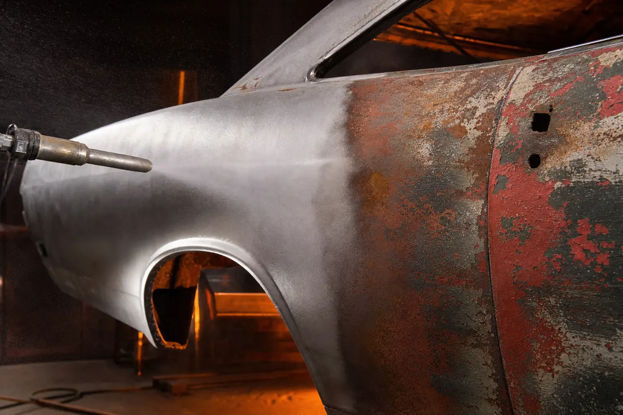 Classic muscle car body panel mid-blasting, half stripped to bare metal, half still covered in old paint and rust